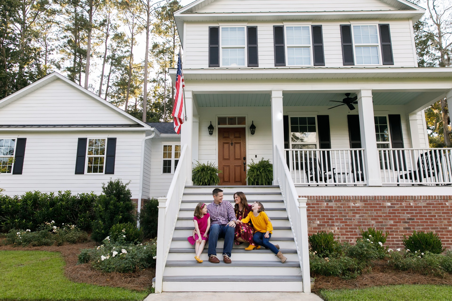 Family standing outside front of new construction white siding farmhouse in the suburbs